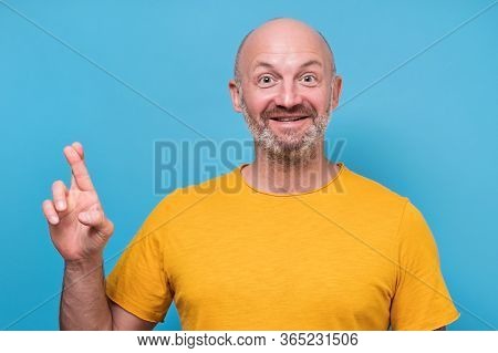Hopeful Mature Male Lookingat Camera With Fingers Crossed Making A Wish.