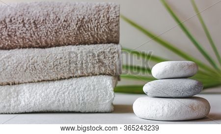 Three Grey Roundstones And Bath Towels On White Background With Green Leaves. Spa Stones, Zen Like C