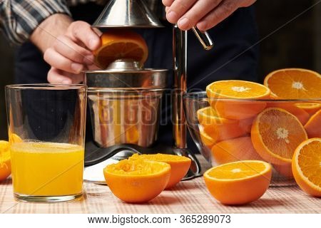 Squeezing an orange with a manual press, close view, making a glass of fresh. Fresh oranges on a wooden table, whole, squeezed and sliced.
