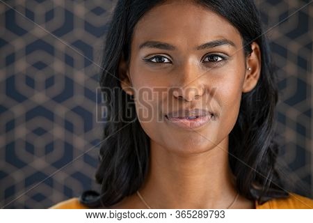 Portrait of young beautiful indian woman smiling and looking at camera. Close up face of happy woman with satisfaction in the eyes. Middle eastern girl standing on pattern background with copy space.