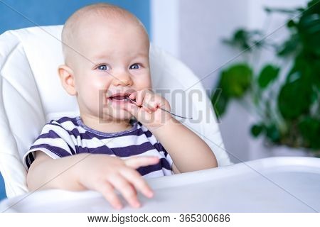 Baby Food. Little Smiling Caucasian Child With Spoon In His Mouth On Highchair. Two First Milk Tooth