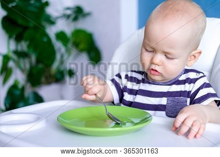 Baby Food. Little Serious Caucasian Child With Spoonand Empty Green Plate On Highchair. Newborn Infa
