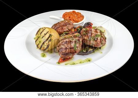 Tasty Pork Meatballs With Ljutenica, Potato, And Spices On A Plate, Isolated On Black Background