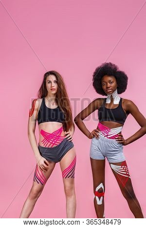 Kinesiology Taping. Two Young Female Athletes On Pink Background With Kinesiology Tape On Neck, Shou
