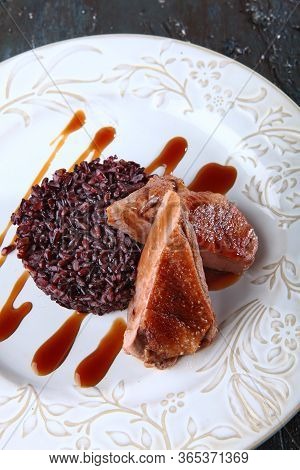 Duck With Brown Rice On A White Plate. Macro Photo On A Dark Textured Background. Copy Of The Space.