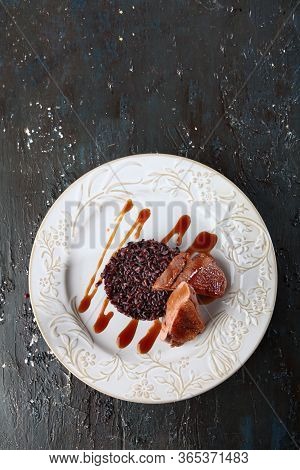 Duck With Brown Rice On A White Plate. Photo On A Dark Textured Background. Copy Of The Space.