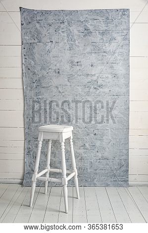 White High Wooden Stool With A Grey Textured Background. Bar Chair In White Wooden Minimalist Room. 