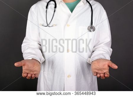 Doctor In A White Coat With A Stastoscope On A Dark Background Stretch Out Hands And Palms Copy Spac