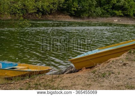 Aft Of One Boat And Bow Of Another On Sandy Shoreline Of River.