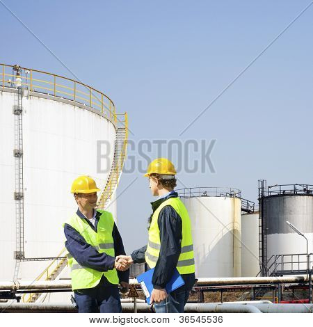Dwóch pracowników przemysłu ropy naftowej drżenie rąk przed zbiorników petrochemicznych refinary