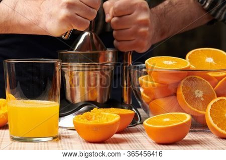 Squeezing an orange with a manual press, close view, making a glass of fresh. Fresh oranges on a wooden table, whole, squeezed and sliced.