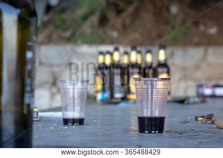 Two Almost Empty Cups Of Wine. Blurred Beer Bottles In The Background. Remains Of Rubbish And Trash 