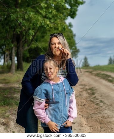 Happy Young Mother And Daughter Smile And Kiss In Nature On A Warm Sunny Day On Mother's Day.