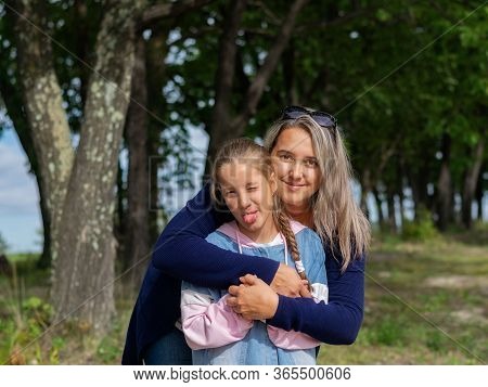Happy Young Mother And Daughter Smile And Kiss In Nature On A Warm Sunny Day On Mother's Day.
