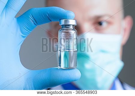 Close Up Hand Of Doctor In Blue Latex Glove And Medical Gauze Mask With Glass Ampoule. Health And Va