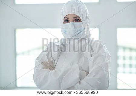 Medical Worker In Protective Clothing And Medical Mask Standing With Her Arms Folded