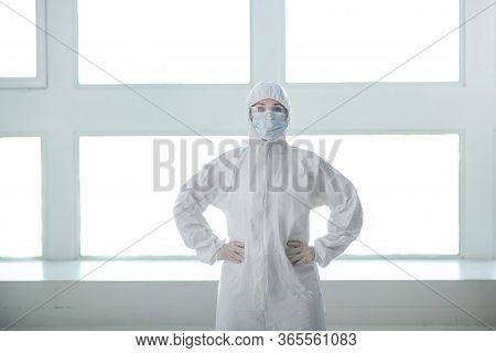 Medical Worker In Protective Clothing, Medical Mask And Goggles Standing With Her Hands On Her Waist