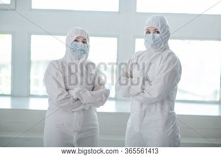 Medical Workers In Protective Clothing And Medical Masks Standing With Their Arms Folded