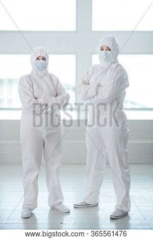 Medical Workers In Protective Clothing And Medical Masks Standing With Their Arms Folded