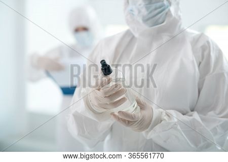 Close-up Of Medical Worker Hands Holding Antiseptic Bottle, Her Colleague Standing Behind With Clip 