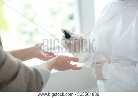Close-up Of Medical Worker Hands Spraying Antiseptic On Female Hands