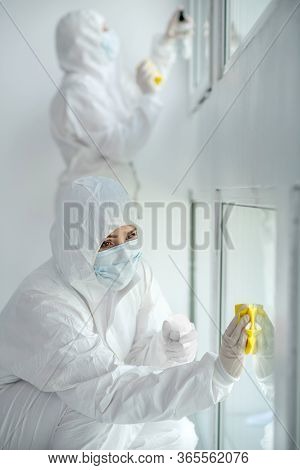 Medical Workers In Protective Clothing And Medical Masks Disinfecting Window