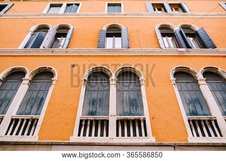 Tall Arch Windows In An Orange High-rise Building In Venice, Italy. Blue Wooden Shutters On Wooden O