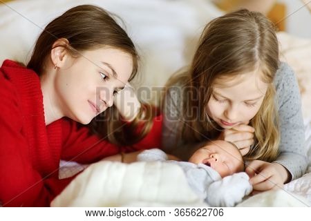 Two Big Sisters Admiring Their Sleeping Newborn Brother. Two Young Girls Holding Their New Baby Boy.