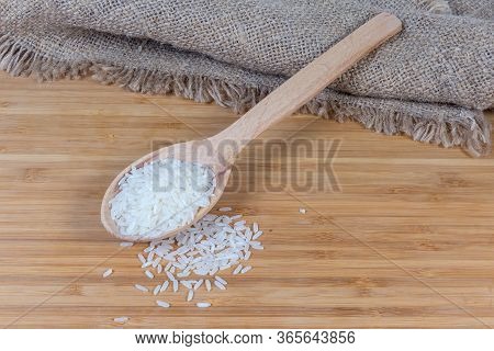 Uncooked Long Grain Basmati Rice In The Wooden Spoon On And Scattered Beside On The Wooden Surface W
