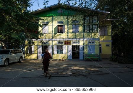 Amarapura, Mandalay, Myanmar - January 14, 2020: Mahagandayon Monastery, buddhist monk studying with book outside near yellow building located on territory of monastery