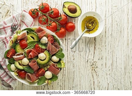 Healthy Lettuce Salad With Prosciutto, Avocado, Tomato And Mozzarella On Wooden Table Background. He