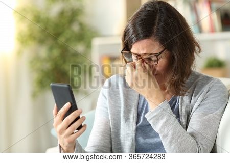 Adult Woman Suffers Eyestrain With Eyeglasses And Holding Phone Sitting On A Couch At Home