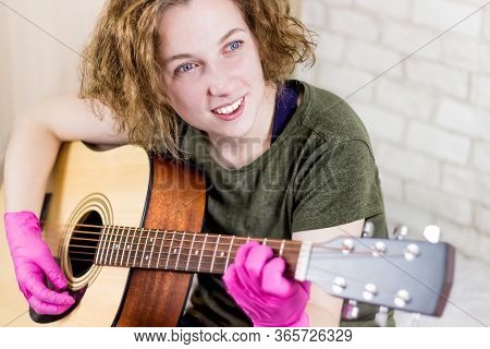 A Young Teenage Girl Smiles And Plays The Guitar In Rubber Gloves And Learns Chords Or A Song. Getti