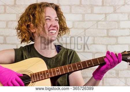 A Young Teenage Girl Smiles And Plays The Guitar In Rubber Gloves And Learns Chords Or A Song. Getti
