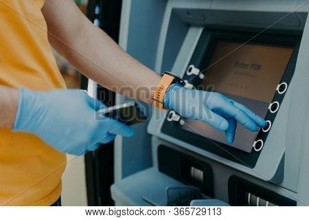 Cropped Shot Of Man Wears Protective Rubber Gloves, Uses Atm Machie To Withdraw Money, Prevents From