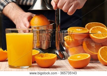 Squeezing an orange with a manual press, close view, making a glass of fresh. Fresh oranges on a wooden table, whole, squeezed and sliced.