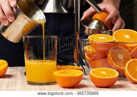 Squeezing an orange with a manual press, close view, making a glass of fresh. Fresh oranges on a wooden table, whole, squeezed and sliced.