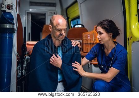 Nurse Talking Friendly With A Patient Sitting In A Blanket In An Ambulance Car