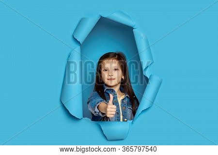 Portrait Of Cute Happy Smiling Caucasian Little Cild Girl Showing Thumbs Up In Blue Paper Hole.