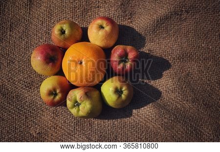 Top View Of Orange Amid Apples With Water Droplets Isolated On Burlap Background In Horizontal Orien