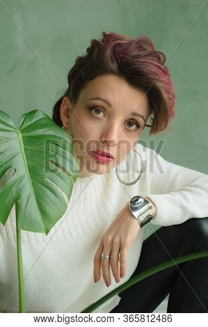Beautiful Lady In White Sweater, Silver Earrings, And Braclet Sitting Near Green Palm Tree And Looki
