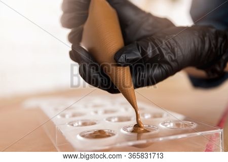 Chef Or Chocolatier Pouring Melted Dark Chocolate Into Silicone Molds On Pastry Bag
