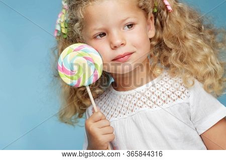 A Child With A Candy. Little Girl With A Round Candy In The Studio On A Blue Background.
