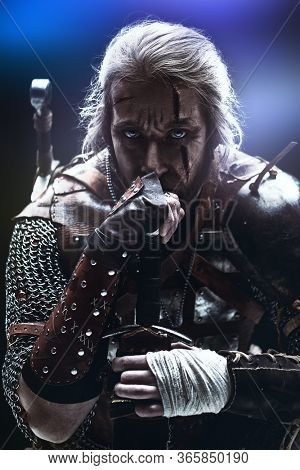 Portrait of a brave medieval warrior in armor with a sword on a black background. The Witcher man.