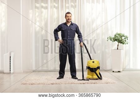 Full length portrait of a male worker in a uniform with a vacuum cleaner in a house