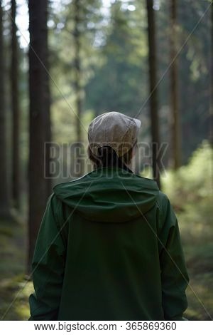 Unrecognisable Man In A Green Jacket And Cap Looks At The Forest.