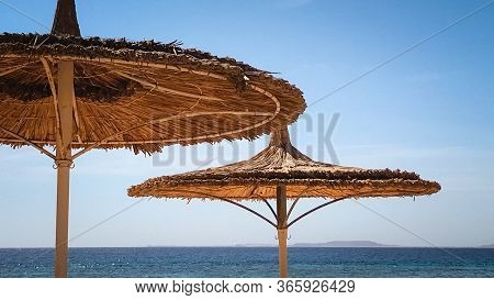 Symmetrical Thatched Beach Umbrellas On A Sultry Summer Day.