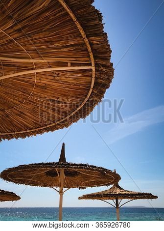 Symmetrical Thatched Beach Umbrellas On A Sultry Summer Day.