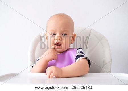 Baby Food. Little Thoughtful Caucasian Baby Girl In Pink Bib On Highchair At Home Over White Backgro