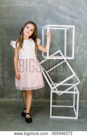Beautiful Little Girl With Broun Long Hair On A Grey Background Near The White Constructure Of The C